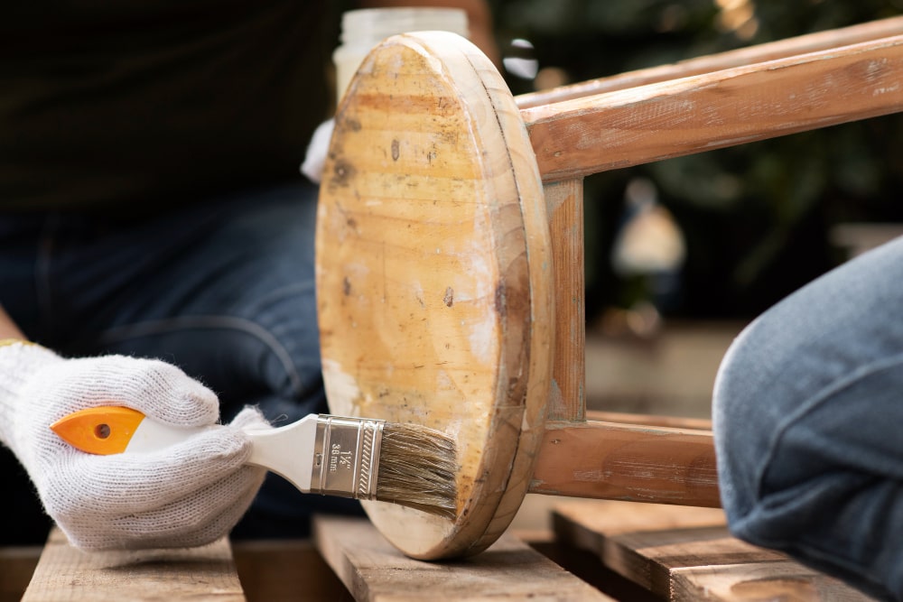 A hand using a brush to paint an old chair, highlighting the restoration process.