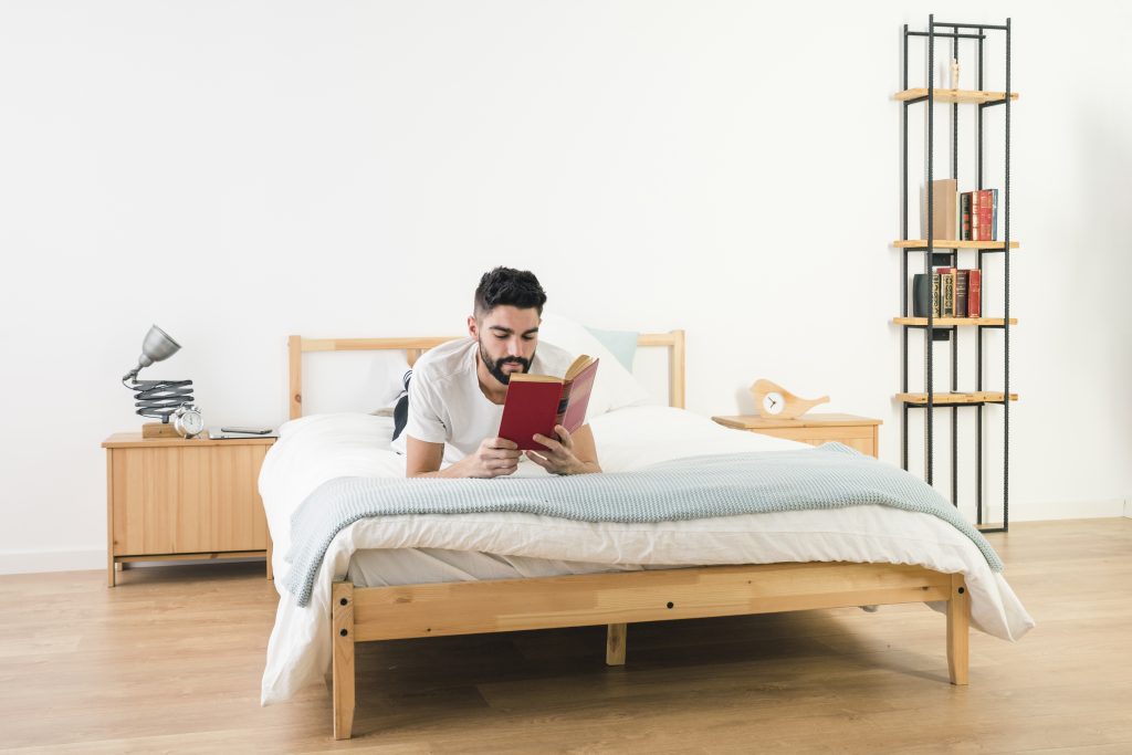 A man lying on a bed in a cozy bedroom, reading a book and enjoying a relaxing moment- furniture on rent